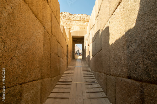 Visitors walk through a stone pathway leading to an ancient structure in Egypt during daylight hours