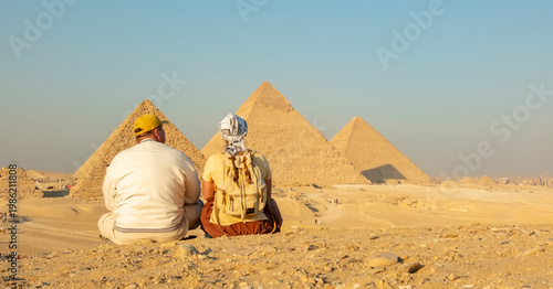 Visitors sit and watch the great pyramids in Giza during golden hour in Egypt
