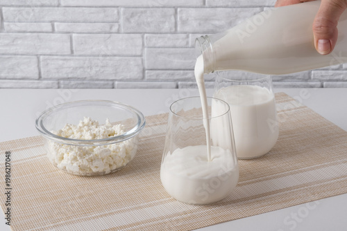 Pouring homemade kefir, buttermilk or yogurt with probiotics. Yogurt flowing from glass bottle on light background. Probiotic cold fermented dairy drink. Trendy food and drink