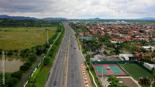 Aerial Forward Tracking Shot Over Highway Between Suburban Neighborhood and Green Fields