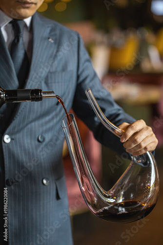 Tableau sur toile Professional sommelier holding glass decanter with red wine during serving proce