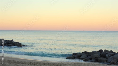 Wide beach view with calm sea gentle waves at pastel sunset