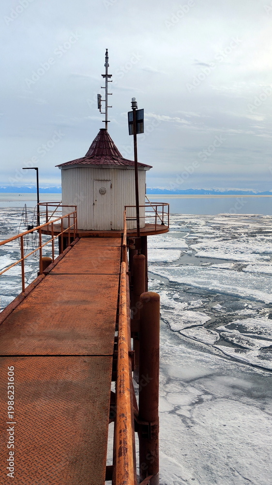 Fototapeta premium Old Rusty Bridge and House on the Shore of Lake with Breaking Ice
