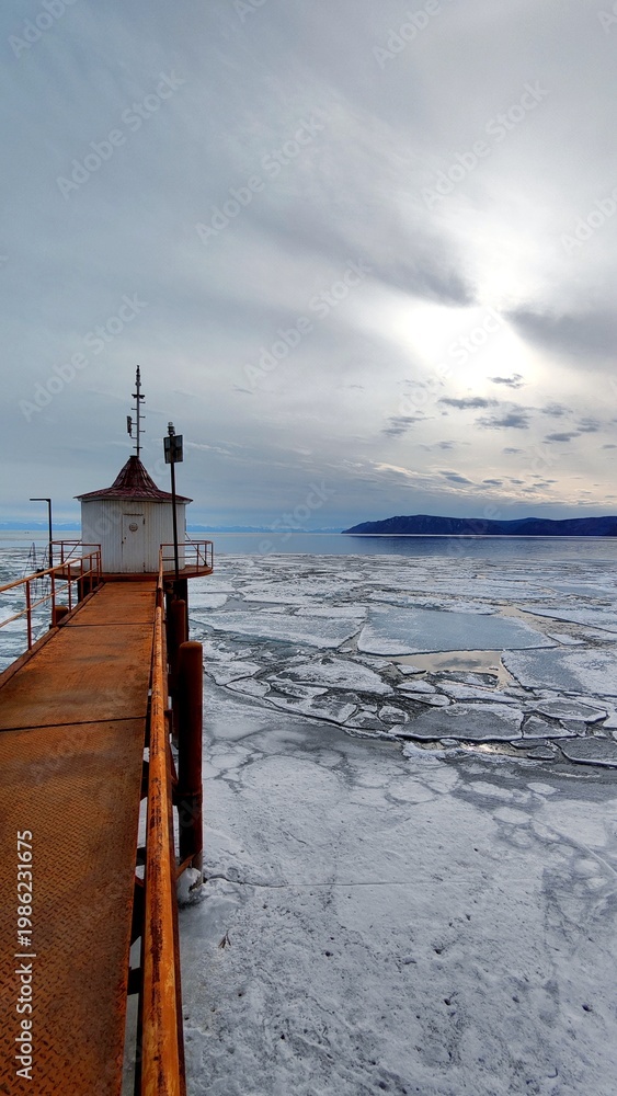 Fototapeta premium Old Rusty Bridge and House on the Shore of Lake with Breaking Ice