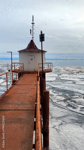 Old Rusty Bridge and House on the Shore of Lake with Breaking Ice