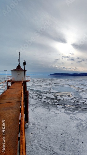 Old Rusty Bridge and House on the Shore of Lake with Breaking Ice