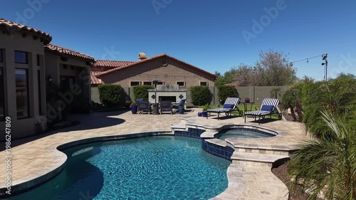 A 4k aerial view of a desert landscaped home in Arizona featuring a travertine tiled pool deck with a fireplace and outdoor kitchen.