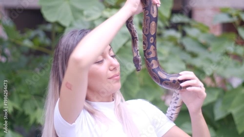 Young woman holding python snake in abandoned urban environment, wild nature concept