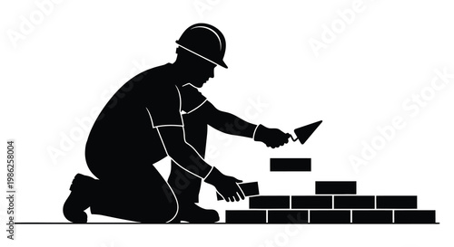 A construction worker kneels and applies mortar to bricks during wall building