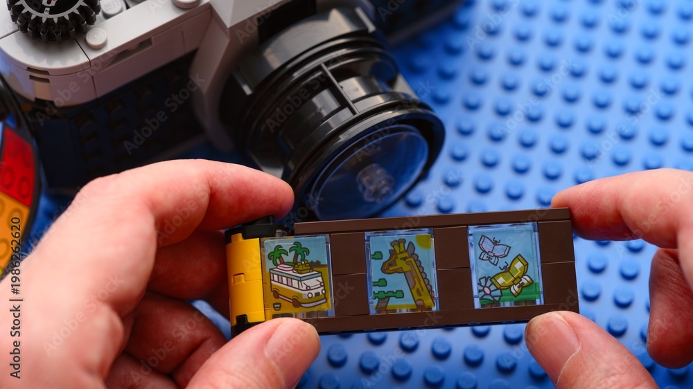 Fototapeta premium Tambov, Russian Federation - February 20, 2026 Person hands holding a toy film strip from the Lego Creator 3in1 Retro Camera building set with a vintage-style brick-built camera on the background.