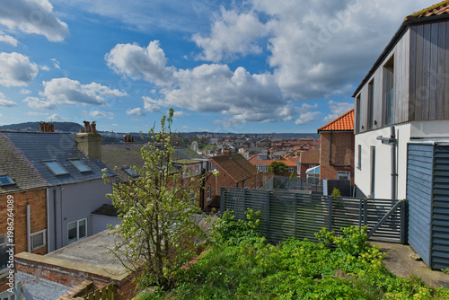 An elevated scenic view of a town under a partly cloudy sky. Residential buildings and green foliage are in the foreground in Scarborough - Yorkshire - Great Britain