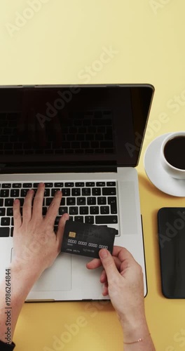 Vertical video: User's hands are typing card info on laptop at yellow desk as checkout opens to pay