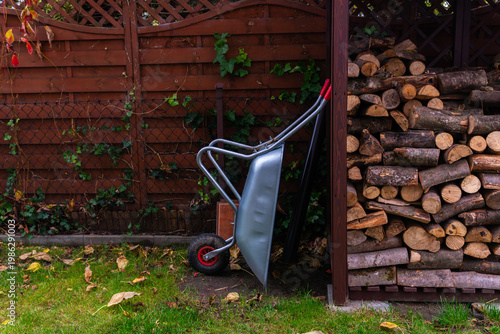 Firewood stack wheelbarrow backyard shed wood logs rural lifestyle heating energy preparation sustainable fuel concept with wooden pile and garden environment rustic countryside outdoor scene