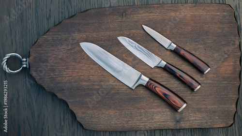 Tableau sur toile Three kitchen knives placed on a wooden cutting board with a ring on the side in