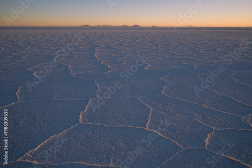 Wide angle view of the Salar de Uyuni salt flats in Bolivia at sunset, featuring the iconic hexagonal salt crust patterns under a colorful twilight sky