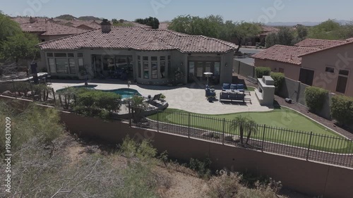A 4k aerial view of a desert landscaped home in Arizona featuring a travertine tiled pool deck with a fireplace and outdoor kitchen.