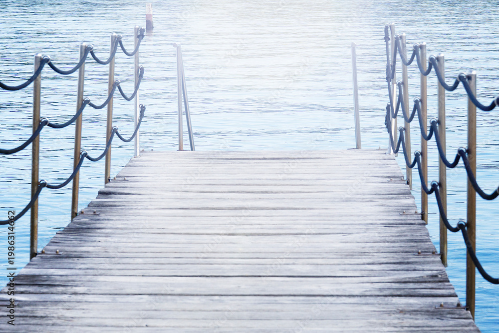 Obraz premium wooden pier bridge blue calm water surface rope railing bright sun light effect on lake horizon with copy space for banner design concept of travel, tourism, architecture