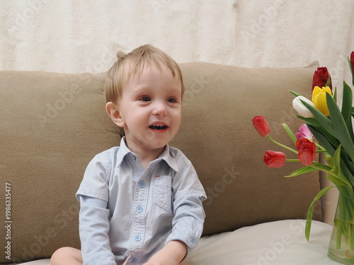Beautiful young boy with tulips flowers and gift box. A gift for mom in a small red box from her son. Happy Mother's Day