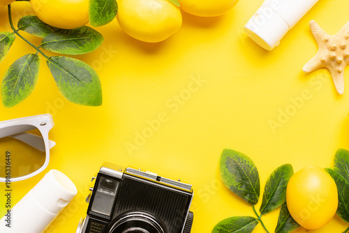 Bright border made with lemon branches, vintage camera, SPF cream, decorative starfish and sunglasses on yellow background top view, copy space for your design. Summer vacation concept.
