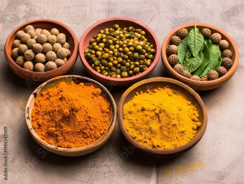 Collection of Ayurvedic herbs and spices in ceramic bowls. Top view of turmeric powder, dried seeds, berries, and fresh green leaves on a stone surface. Holistic medicine concept