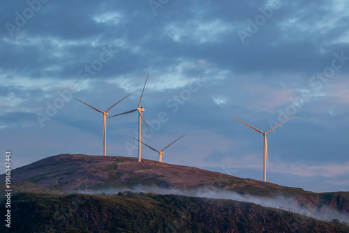 Wind farm on hilltops in Northern Norway at sunrise with dramatic sky and light mist