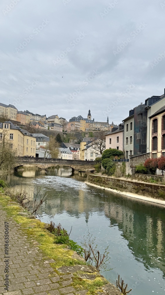 Fototapeta premium Scenic River View of Luxembourg's Old Town with Rainbow Buildings and Stone Bridge