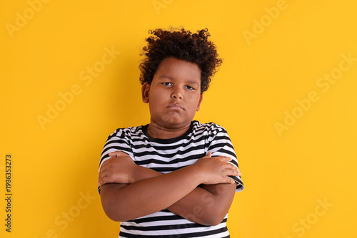 фотографія Portrait of resentful little boy with crossed arms on yellow background