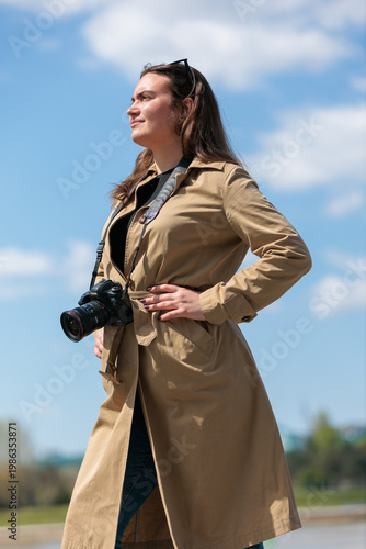 Young woman photographer stands outside and poses with a camera