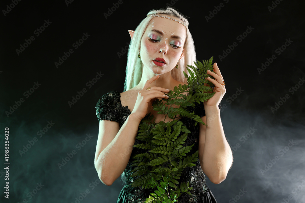 Fototapeta premium Beautiful elf girl with floral decor on black background with smoke