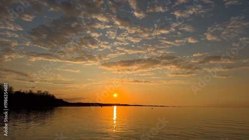 Fotografía Golden sunset sky with scattered clouds over a calm sea
