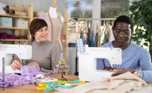 Foto Positive male and female dressmakers stitching garments at machines, working tog
