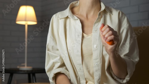 Woman compressing hand expander for wrist rehabilitation. Young woman's hand squeezing a rubber ring expander for exercise, strengthening her grip and forearm muscles in a calm home setting