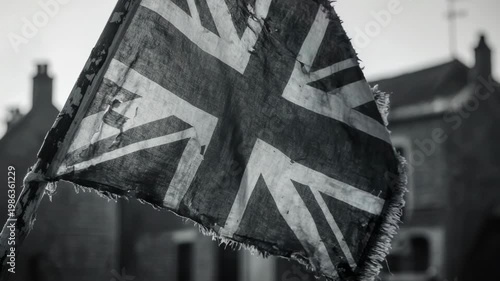 Tattered Union Jack flag waving in black and white. Close-up of a worn British flag from the World War II era. Resilience and historical conflict concept