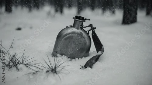 Metal military canteen lying in the snow. Black and white footage of abandoned soldier gear in winter. World War battlefield and history concept