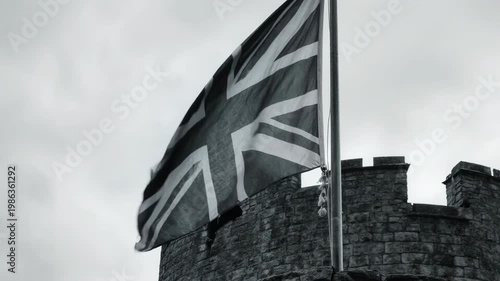 Union Jack flag waving on a stone castle turret. Black and white historical footage of the British flag. First and Second World War military heritage concept