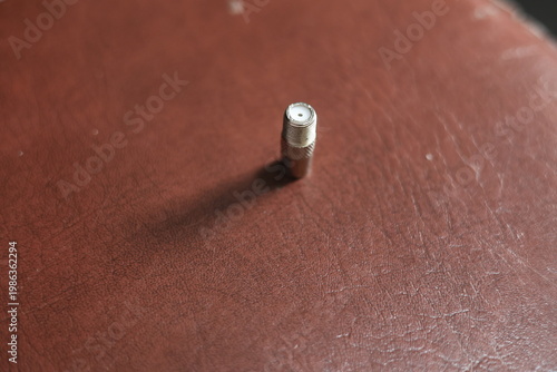 Close-up of a silver coaxial cable connector lying on a textured surface