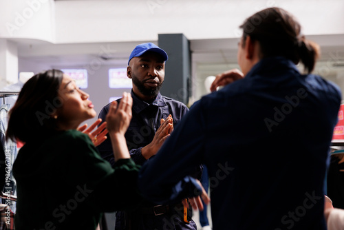 Foto Calm polite African American male security officer managing crowd in shopping mall during sales, asking two angry mad shoppers to remain calm during Black Friday