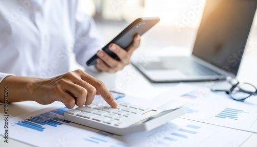 Close-up of hands using a calculator and smartphone, with a laptop and glasses in the background, symbolizing financial planning and analysis