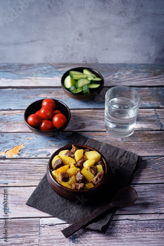 Roasted meat with potato in a bowl on a wood background