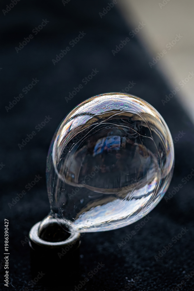 Fototapeta premium A fragile iridescent soap bubble attached to a small metal base against a dark background