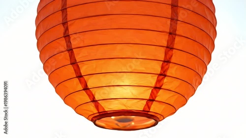 Close-up of a richly colored red orange paper lantern hanging against a stark white background