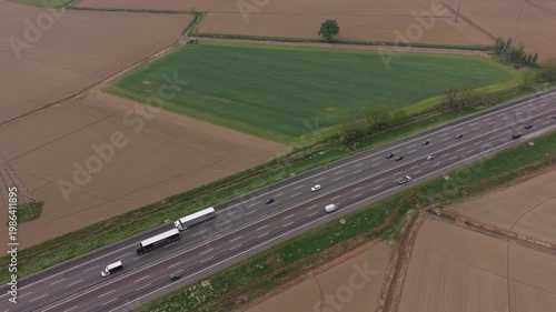 Aerial Highway View: A high-angle drone shot captures a modern highway stretching through vast agricultural fields, with trucks and cars navigating the lanes.