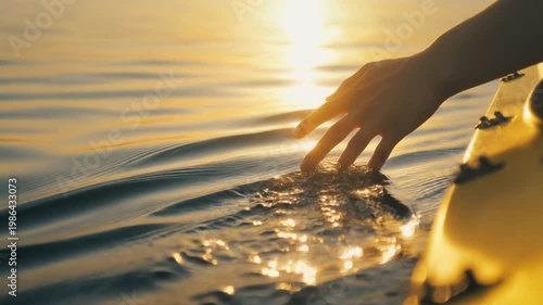 Close-up of a human hand delicately caressing the tranquil ocean surface, illuminated by golden hour sunlight, creating gentle shimmering reflections and soft ripples