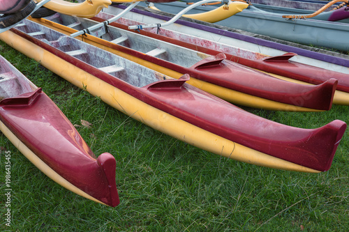 Red and Yellow Outrigger Canoes Resting on Green Grass.