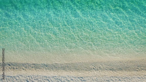 Top down view of soft white sand beach meeting transparent turquoise waters in Greece