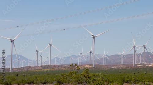 Footage of many large white wind turbines generating clean energy in a wind farm from ground level.