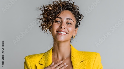 Happy young woman with curly hair wearing a vibrant yellow blazer smiling for a high resolution professional commercial studio portrait photo shot