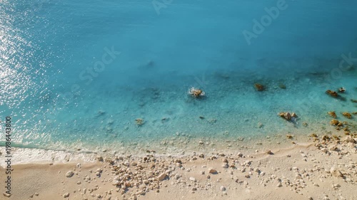 Gentle waves lap a quiet rocky beach where turquoise sea waters meet tan pebbles