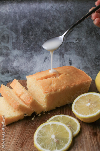 Hand pouring icing glazed on Homemade lemon pound cake on wooden plank. Dessert bakery.