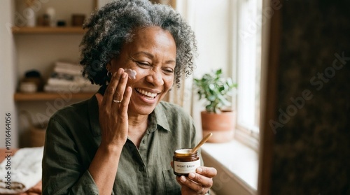 Smiling older black woman with grey hair applying face cream from a jar